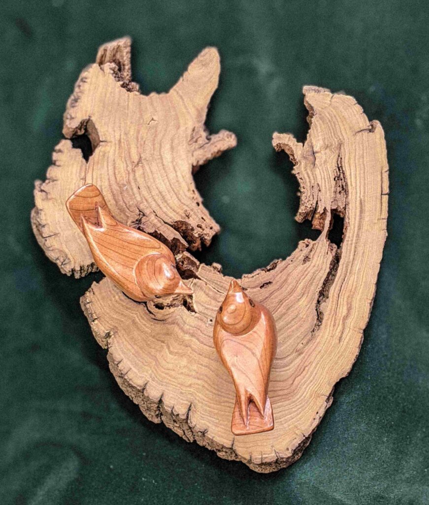 two stylized wood carvings of nuthatches attached to a cross section of chestnut by gary carver of carverscarvings