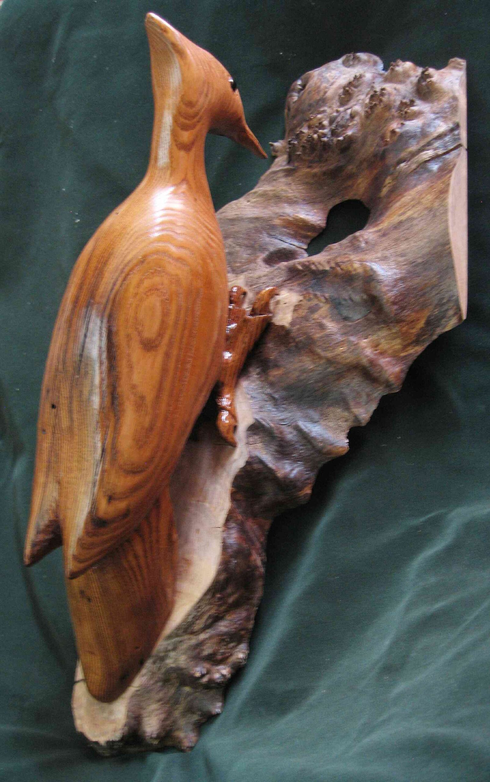 stylized wood carving of a woodpecker mounted a wooden wall hanging by gary carver of carverscarvings