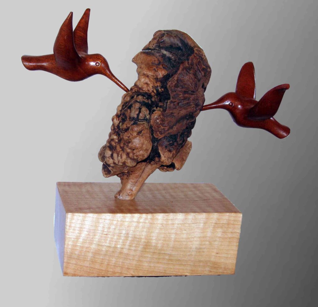 two stylized wood carvings of hummingbirds attached to a wooden burl display by gary carver of carverscarvings