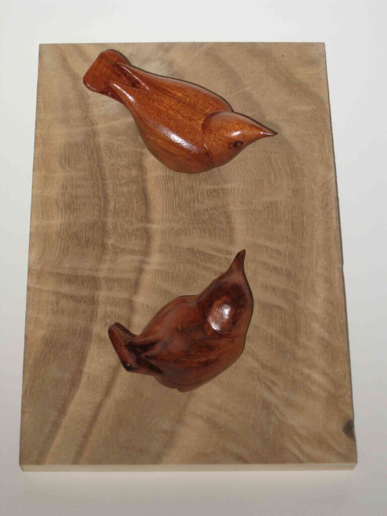 two stylized wood carvings of nuthatches mounted on a wooden paulownia board by gary carver of carverscarvings