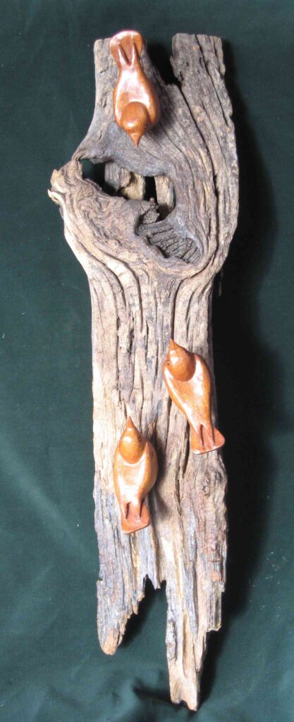 stylized wood carvings of three nuthatches mounted on a wooden wall hanging by gary carver of carverscarvings