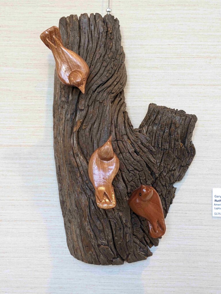 stylized wood carvings of three nuthatches mounted on a wooden wall hanging by gary carver of carverscarvings