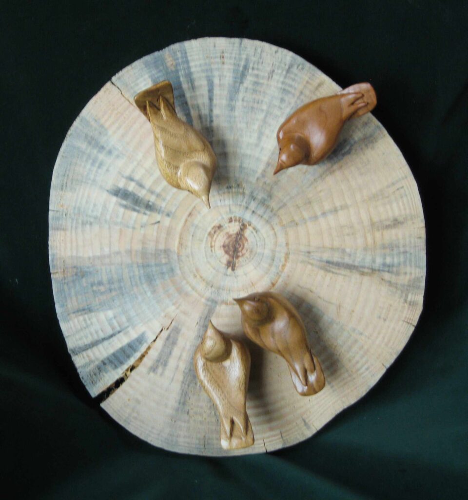 four stylized wood carvings of nuthatches mounted on a round cross section of wood by gary carver of carverscarvings