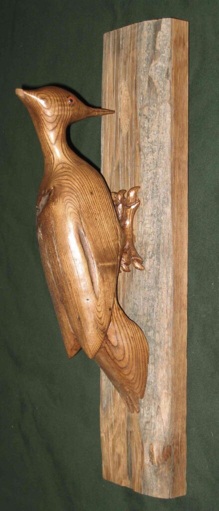 stylized chestnut wood carving of a pileated woodpecker on a wooden board by gary carver of carverscarvings