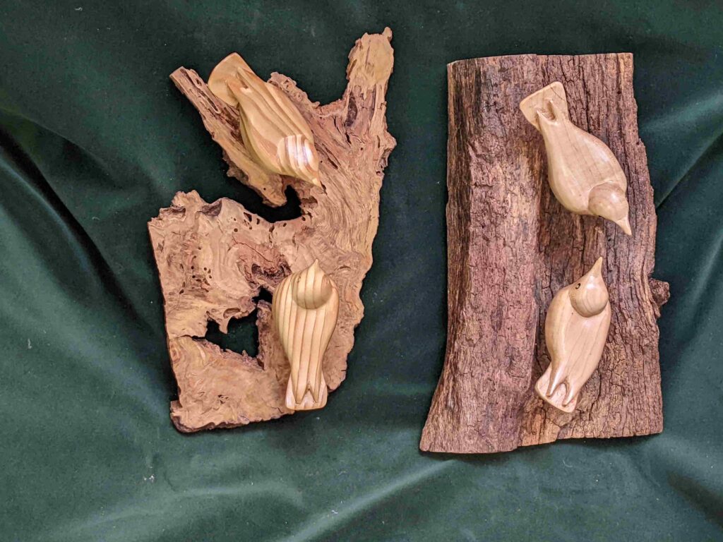 two separate wall hangings each with two stylized chestnut wood carvings of nuthatches